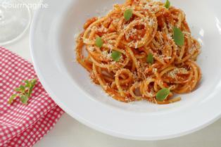 Spaghetti, basil, onions and tomato sauce served on a white plate next to a red napkin