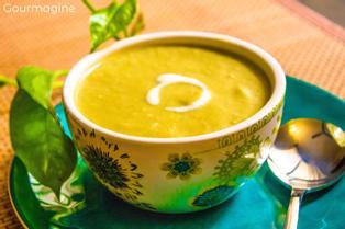 A decorated bowl filled with broccoli cream soup on a blue-green plate