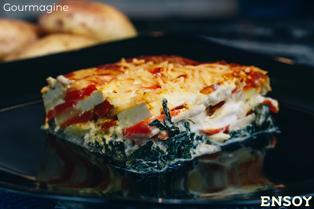 Schwarzer Teller mit einem Stück Kartoffel-Tofu-Auflauf mit veganem Käse darüber geschmolzen