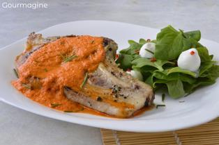 Weisser Teller mit einem Schweinskotelett an oranger Peperonisauce neben grünem Spinatsalat mit Mozzarellakäse