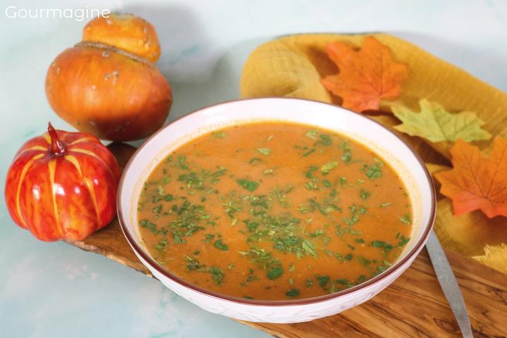 A white bowl with pumpkin soup on a wooden board with pumpkins and leaves