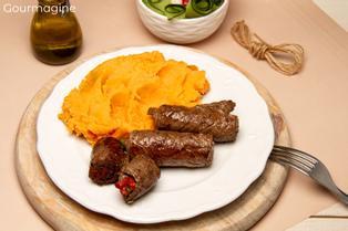 Vier gebratene Plätzli-Rollen gefüllt mit Peperonistreifen angerichtet mit Rüeblipüree auf einem weissen Teller