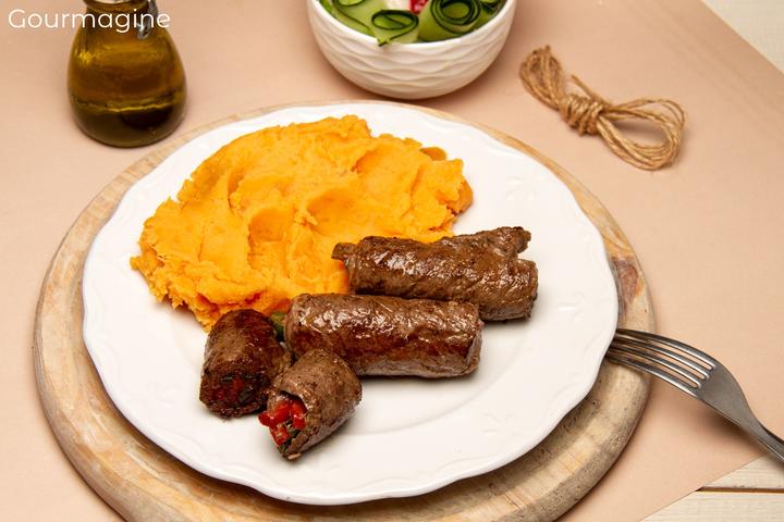 Four roasted schnitzel rolls filled with pepperoni strips served with carrot puree on a white plate