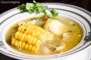 Eine weisse Schüssel gefüllt mit klarer Poulet-Suppe und Maiskolben