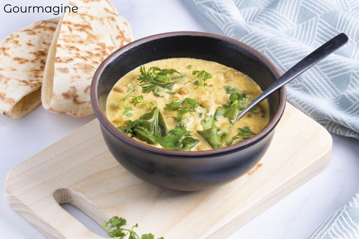 A tomato yoghurt lentil curry served in a black bowl next to two pita breads