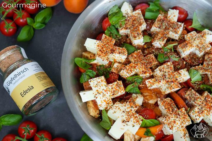 Metal bowl with a mixture of mozzarella, tomatoes, apricots and basil leaves covered in spices and next to a small Gipfelhirsch glass bottle with spices