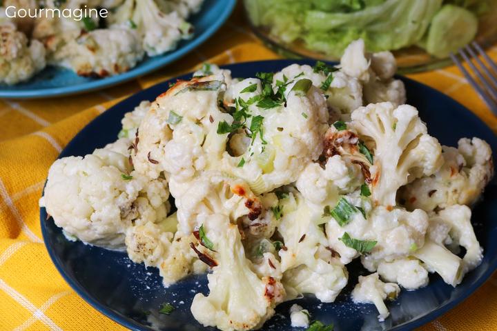 Pieces of cauliflower baked with cheese, onions and parsley on a blue plate