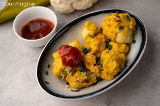 Several baked cauliflower wings on a dark plate next to a white cup of ketchup