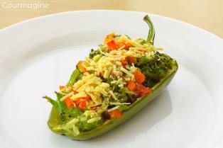 Half of a green pepper filled with broccoli pieces, carrot cubes, tomatoes and small onions covered with Parmesan cheese on a white plate