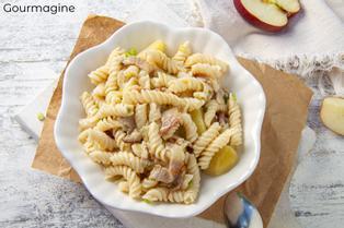Eine weisse Schüssel mit Pasta, Speck und Kartoffeln auf einem Holztisch