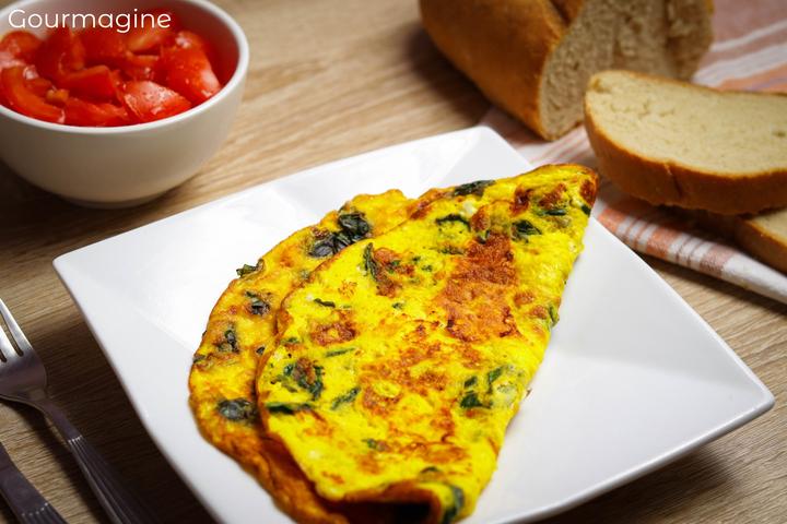 Gelbe und grüne Krautstiel-Omelette auf einem weissen Teller neben einer Schüssel mit Tomaten-Schnitzen und Brotscheiben