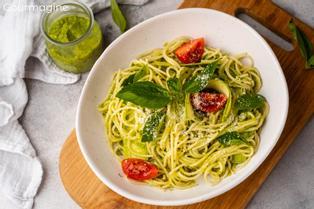 A white bowl filled with spaghetti with pesto and tomatoes