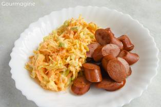 Cabbage carrot salad and a sliced Vienna sausage served on a white plate