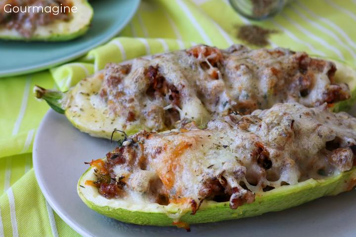 Two halved, hollowed out courgettes filled with minced meat and carrots and topped with cheese on a light blue plate