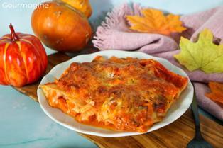 Ein weisser Teller mit Kürbis-Lasagne auf einem Holzbrett mit Kürbissen und Blättern