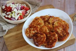 Eine breite weisse Schüssel gefüllt mit Plätzchen aus altem Brot neben einer kleinen Schüssel mit Tomaten, Peperoni, Zwiebeln und Feta
