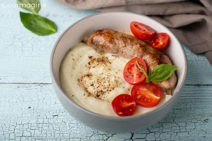 Mehrere geschnittene Tomaten und eine gebratene Wurst angerichtet auf Blumenkohlpüree in einer grauen Schüssel