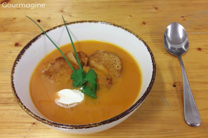 Eine Schüssel mit Kürbissuppe, Brot und Äpfeln auf einem Holztisch dekoriert mit grünen Blättern