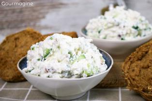 Zwei Schüsseln gefüllt mit Gurken-Käse-Salat neben mehreren dunklen Brötchen